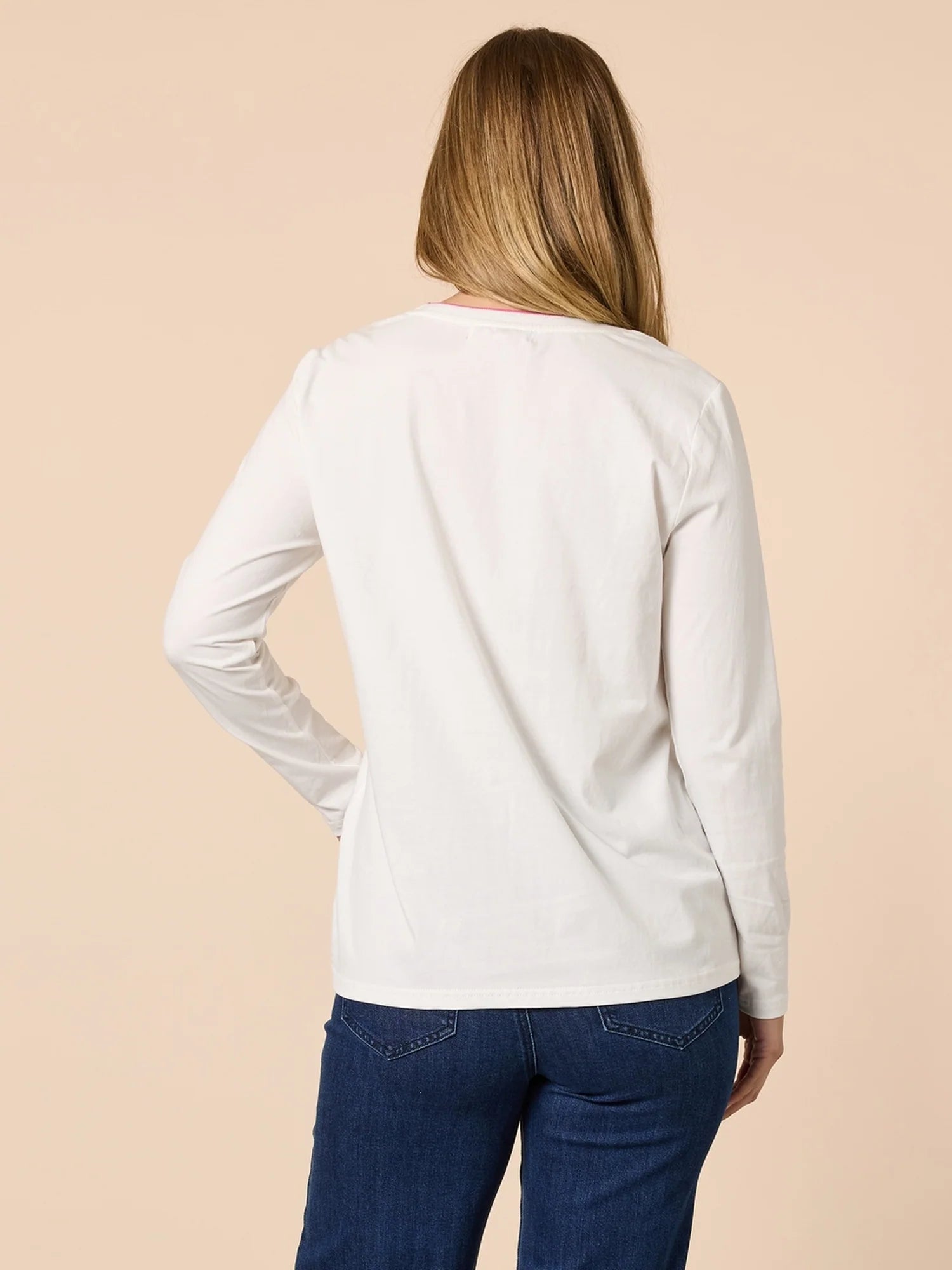 Image of Woman wearing a Threadz white long-sleeve shirt and blue jeans on a beige background