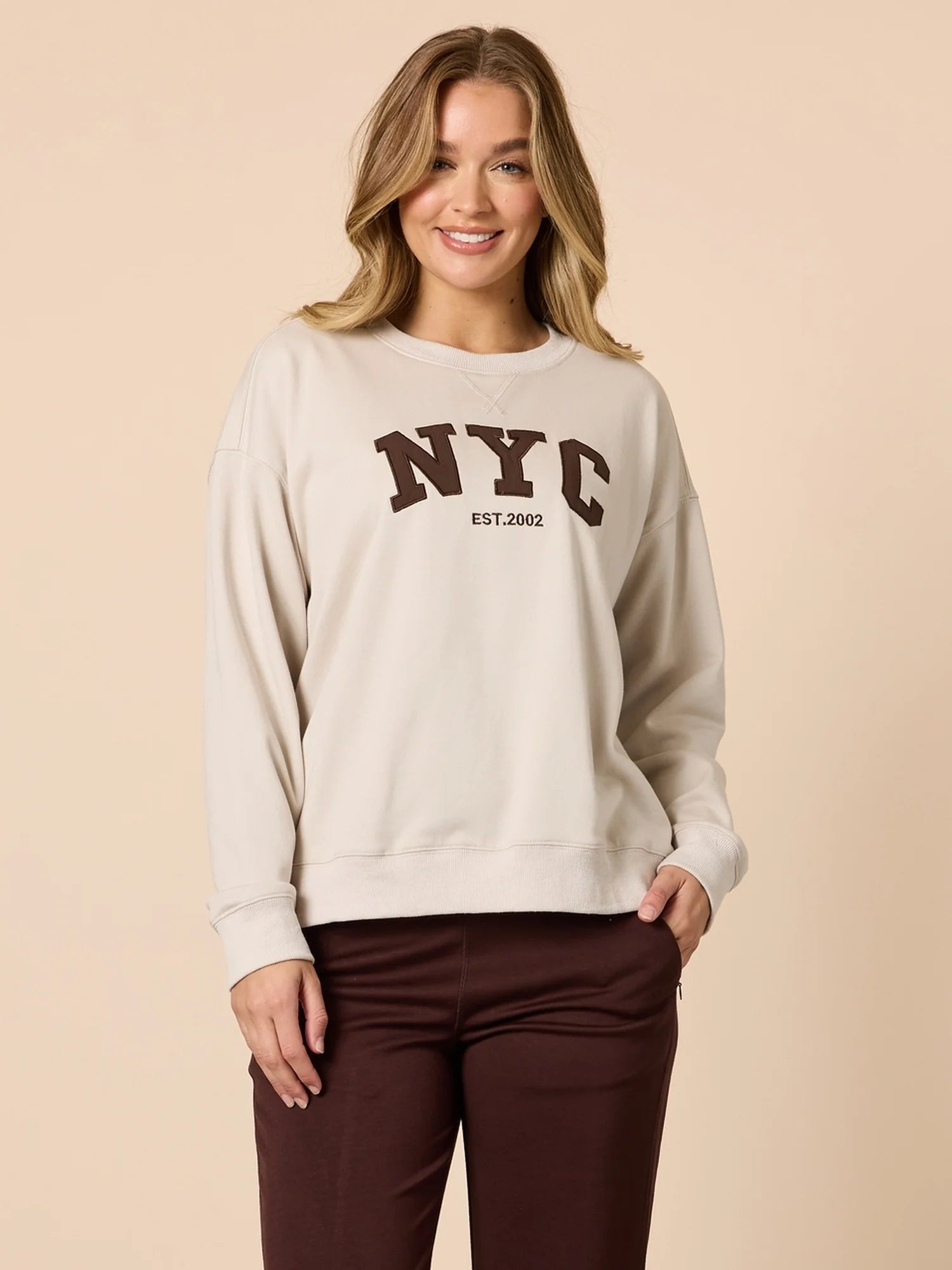 Woman wearing a beige sweatshirt with 'NYC' text on a beige background