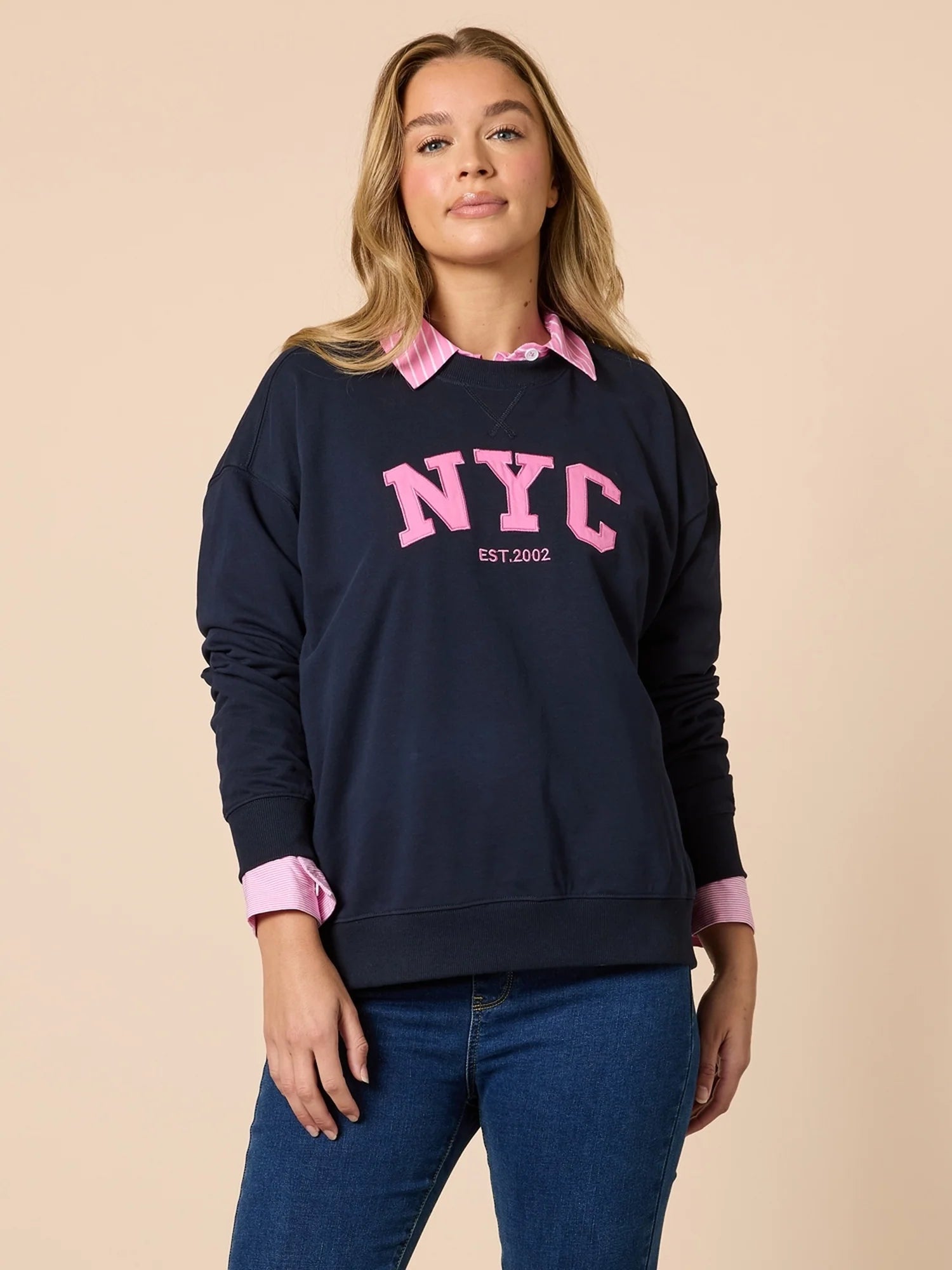 Woman wearing a Threadz navy sweatshirt with 'NYC' in pink text on a beige background