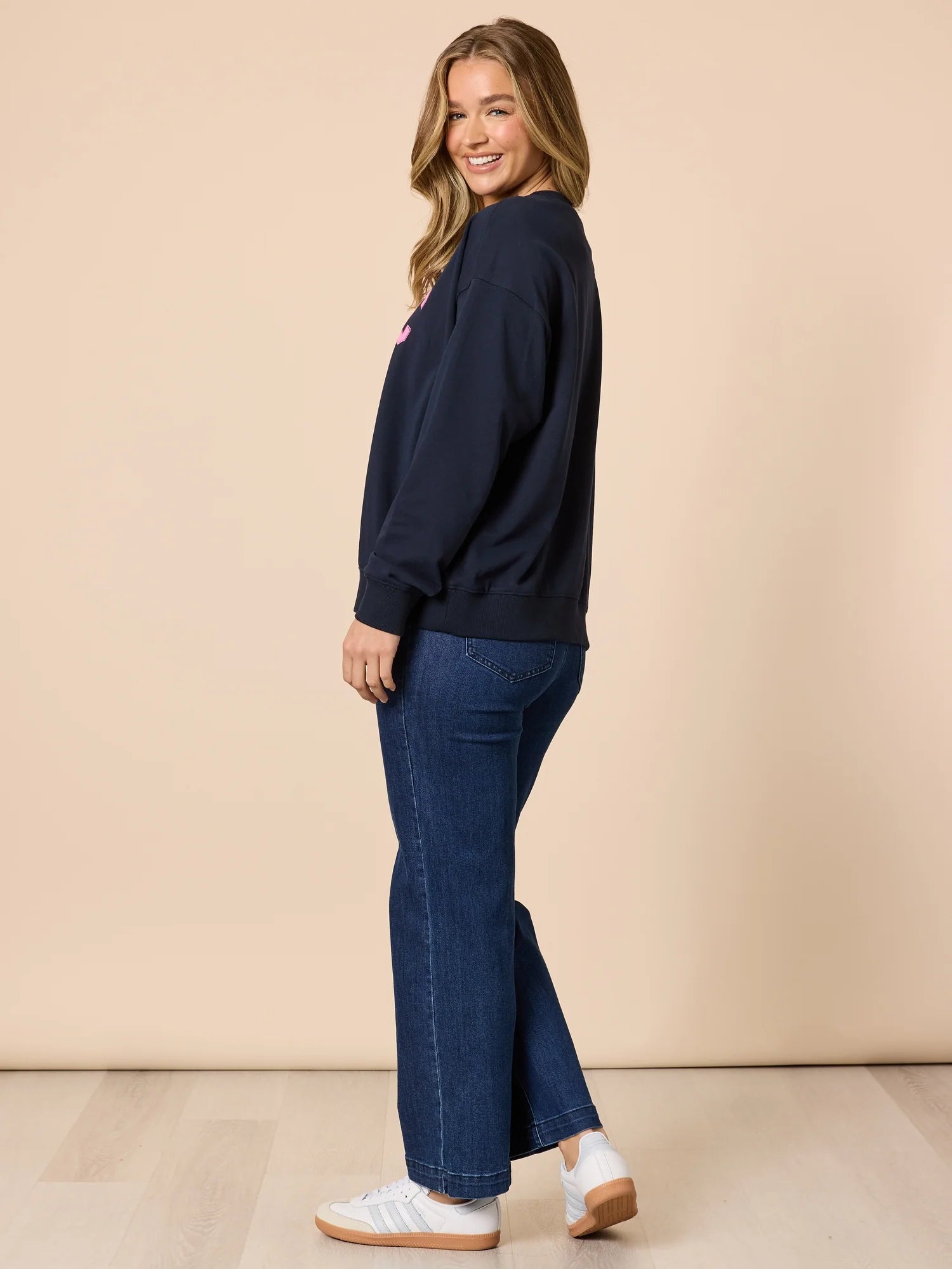 Image of Woman wearing a Threadz navy sweatshirt and blue jeans on a beige background
