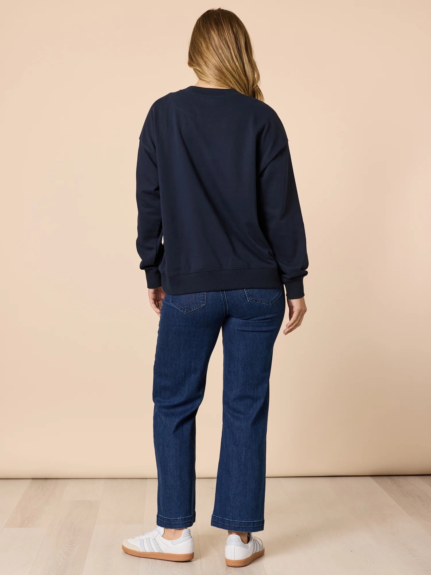 Image of Person wearing a Threadz navy sweatshirt and blue jeans standing against a beige background