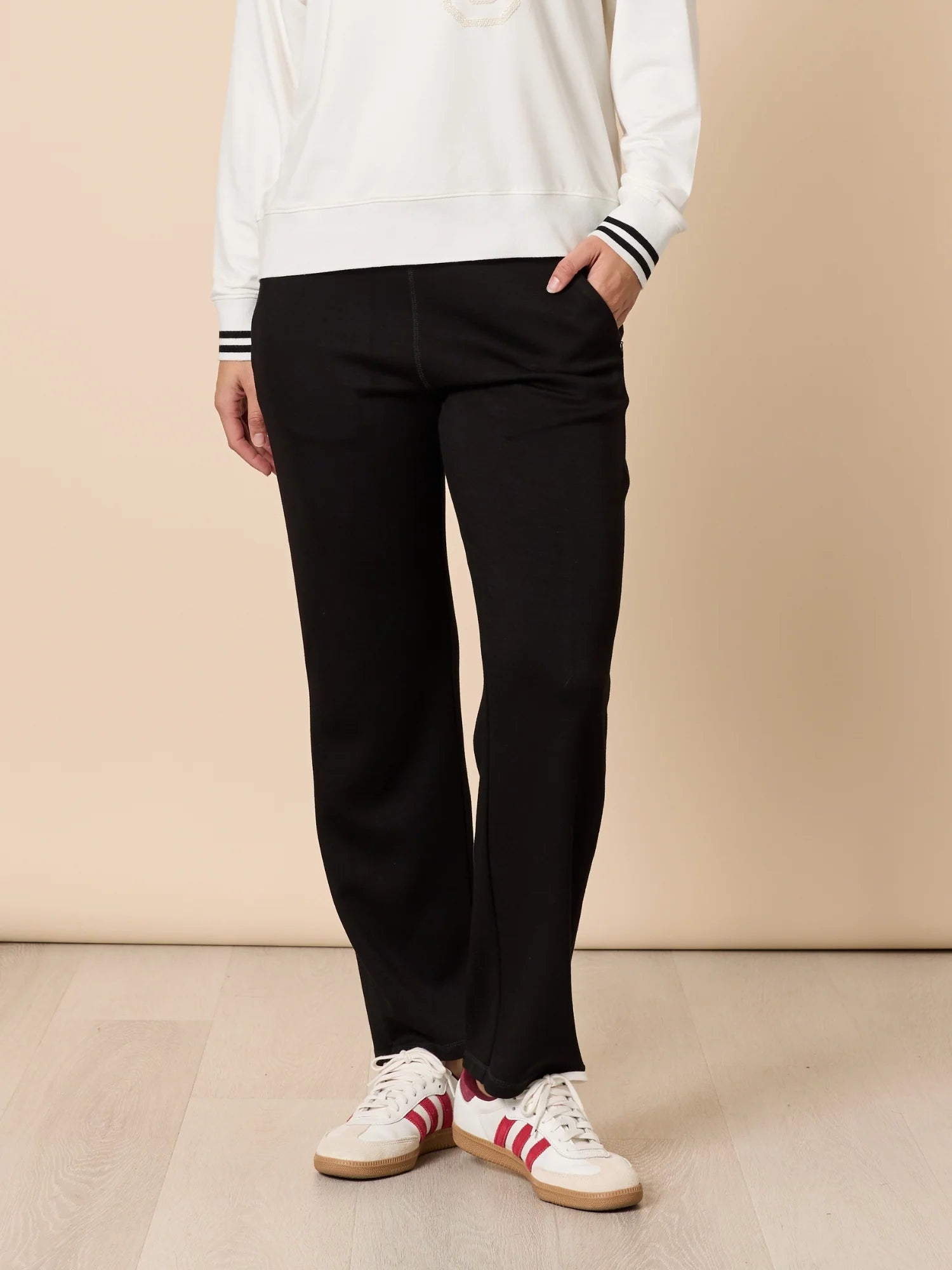Woman wearing Threadz black pants with white and red sneakers on a beige background