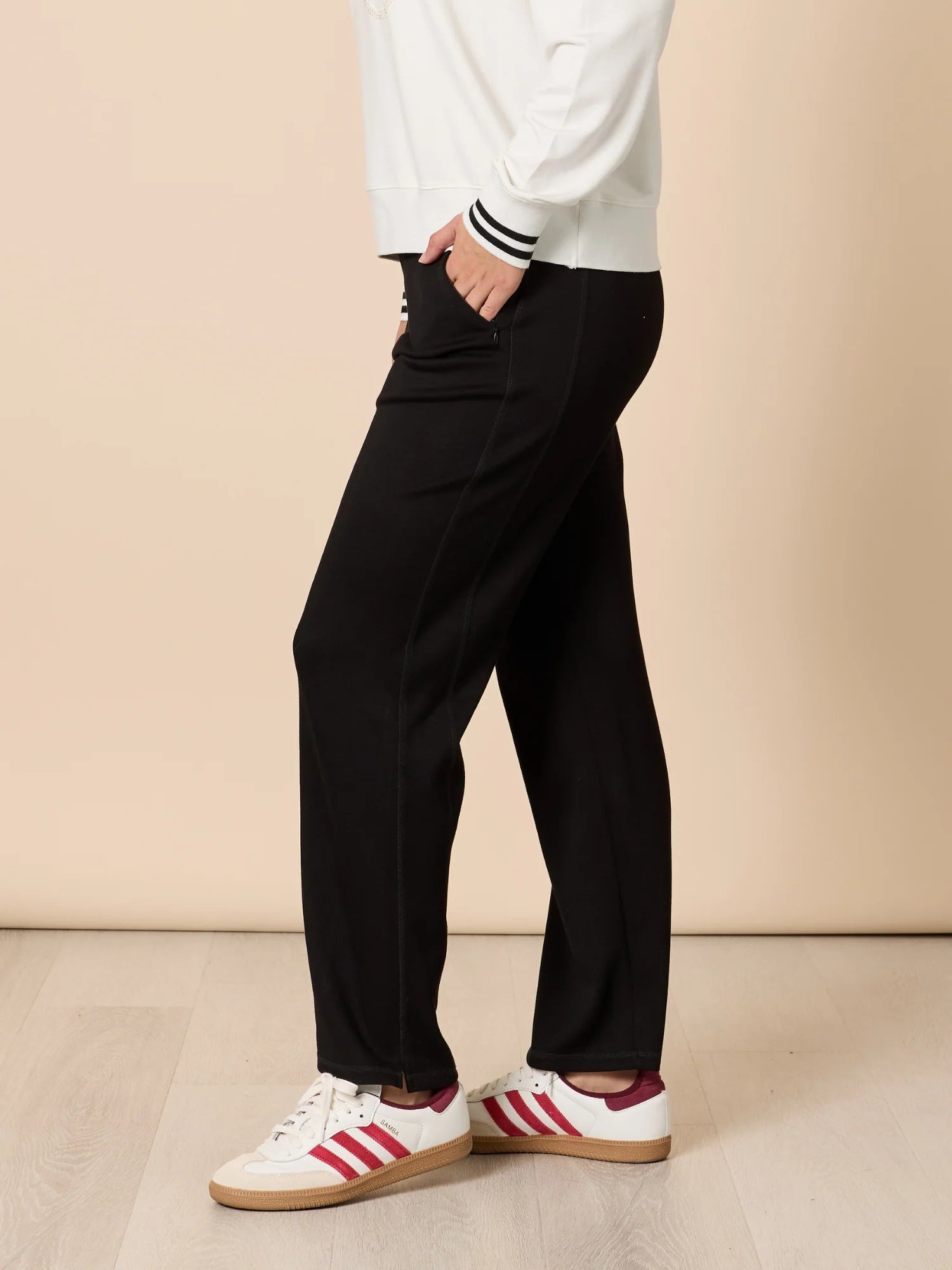 Image of Woman wearing Threadz black pants and white sneakers with red stripes on a beige background