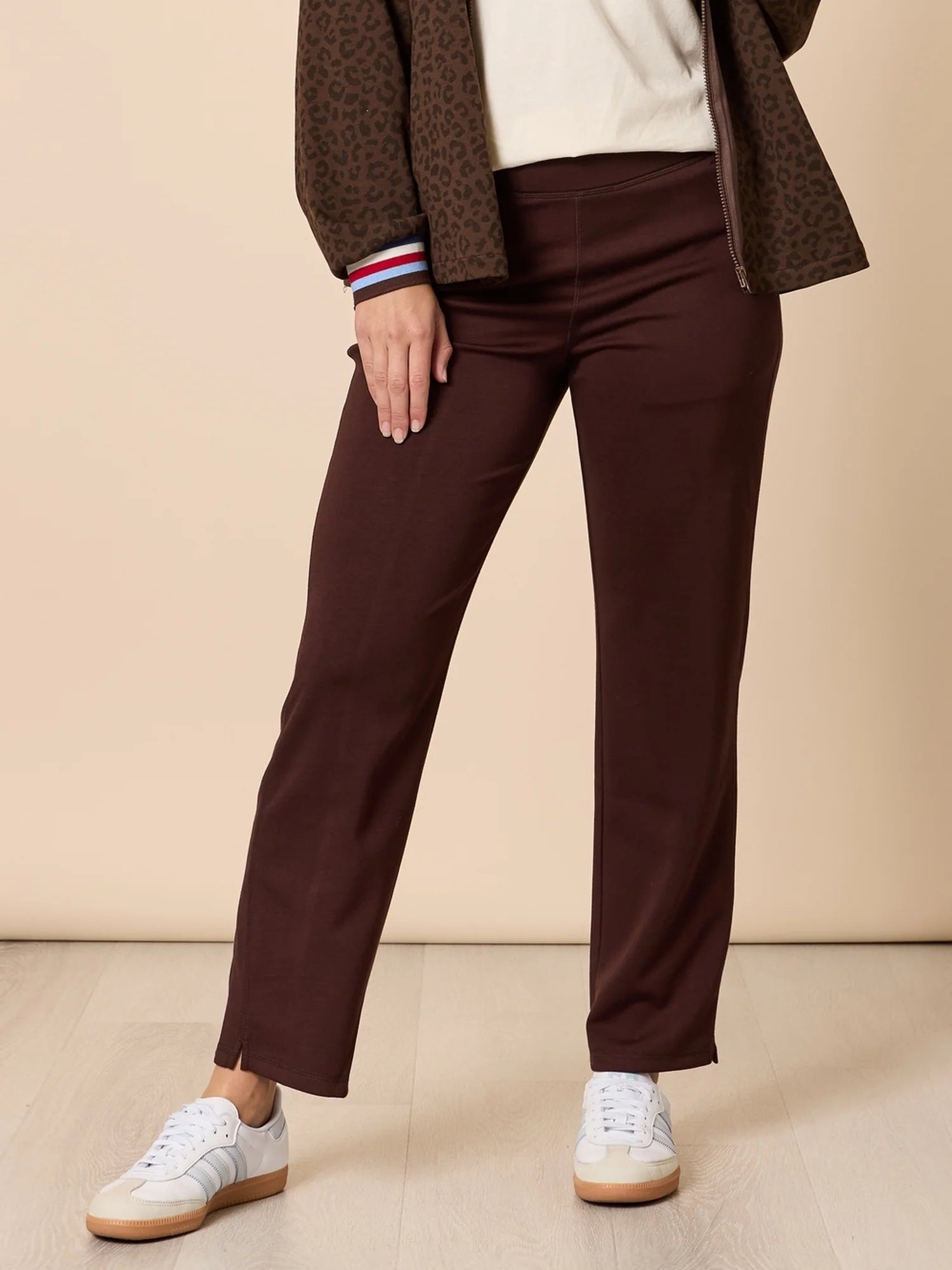 Woman wearing Threadz brown pants and a patterned coat on a beige background