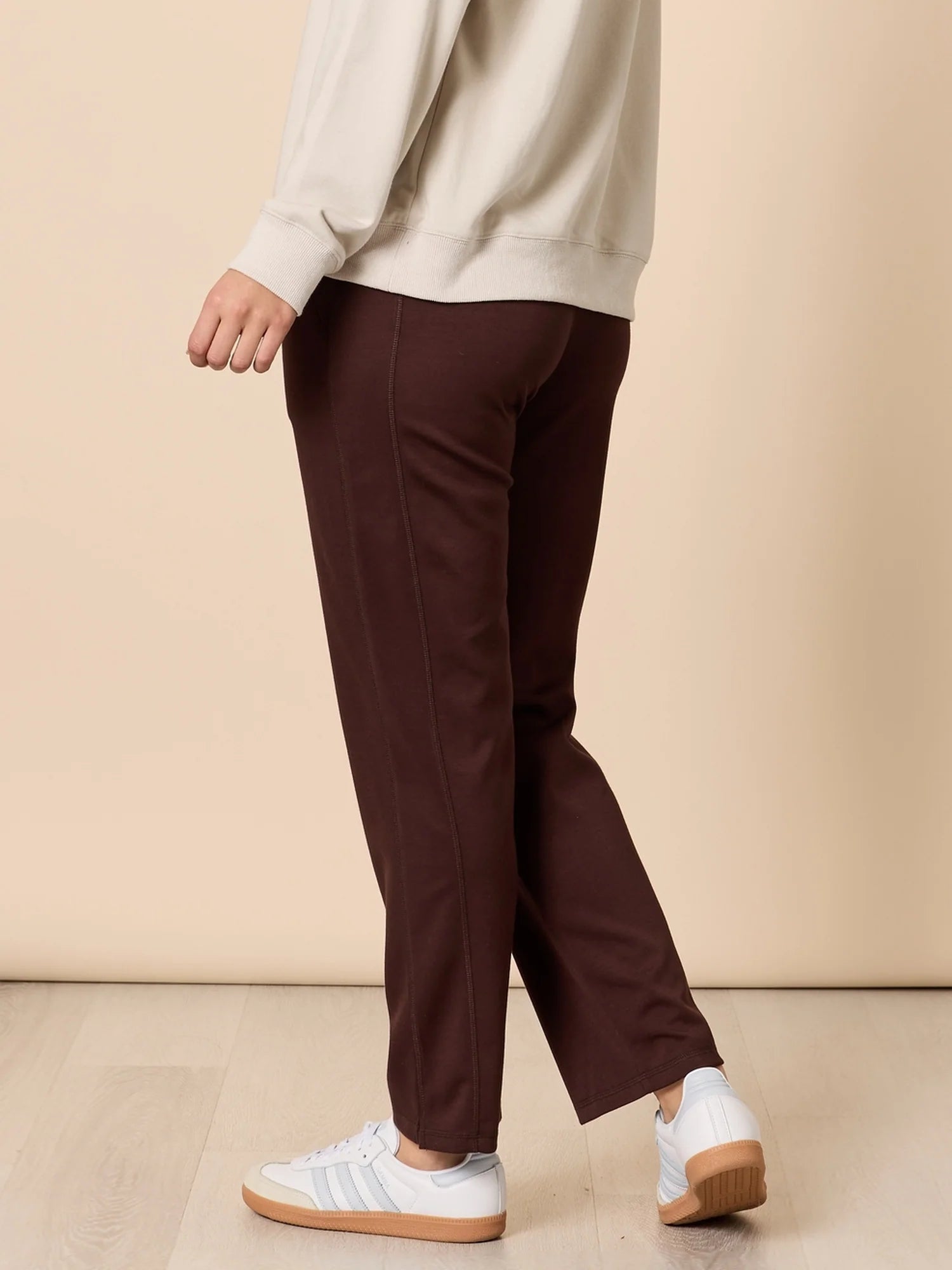 Woman wearing Threadz brown pants and white sneakers on a beige background