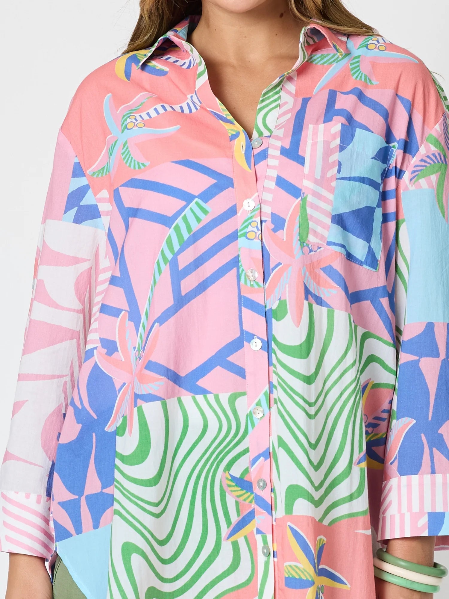 A close-up of a woman wearing a Threadz long-sleeve button-up shirt with a vibrant multicolor patchwork print featuring pink, blue, green, and white tropical and geometric patterns.