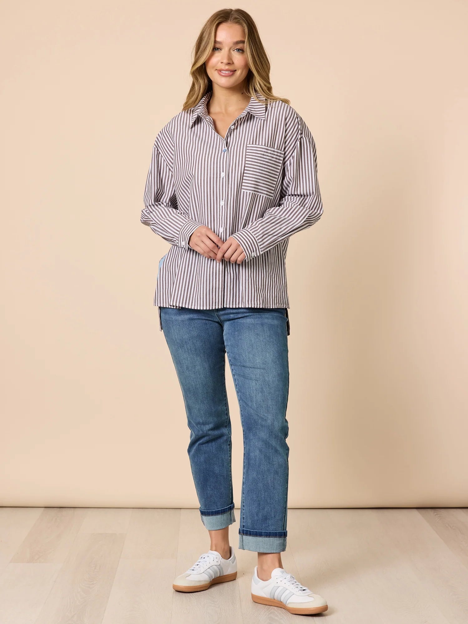 Woman wearing a Threadz striped shirt and jeans against a beige background