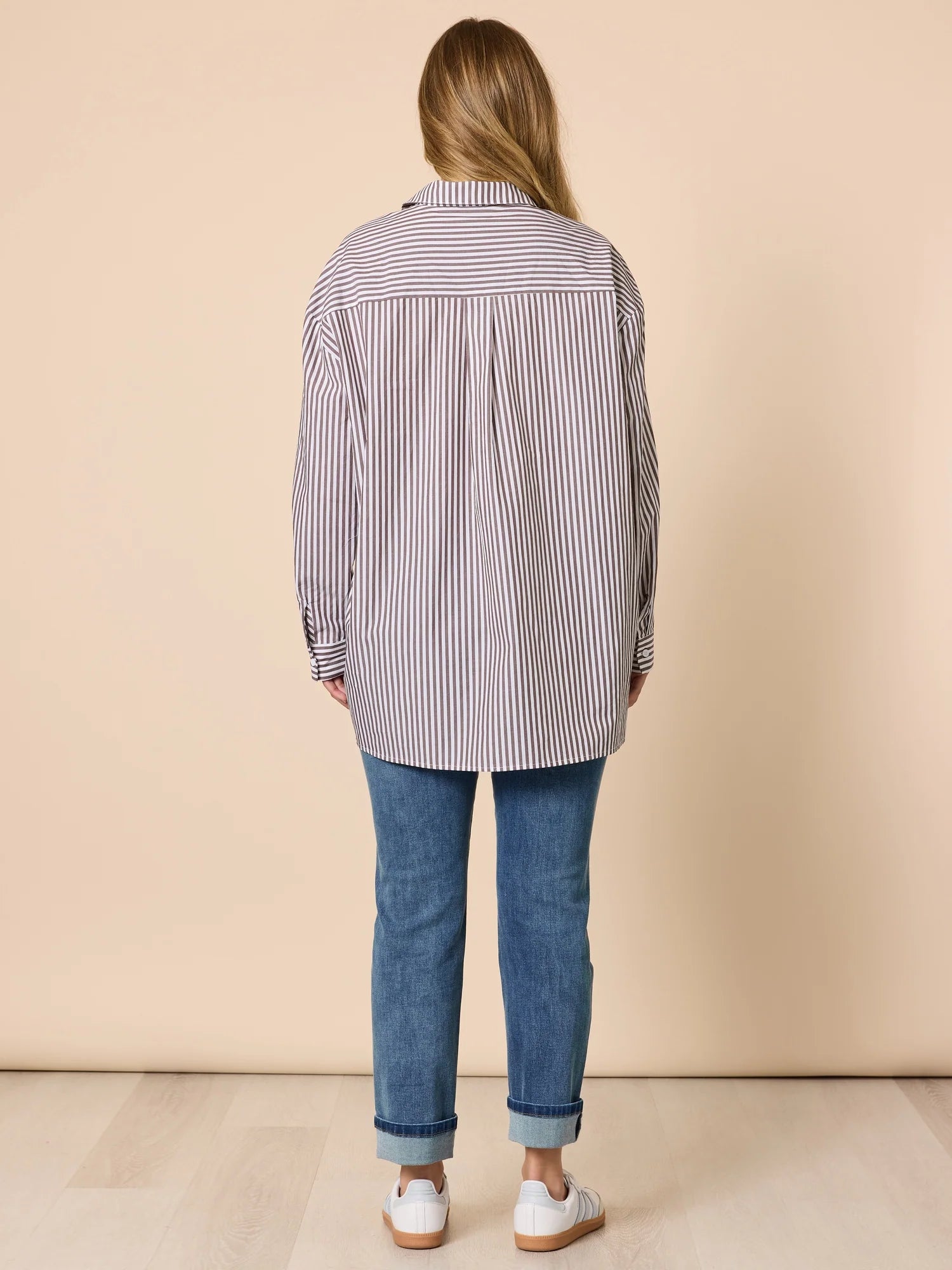 Woman wearing a Threadz striped shirt and blue jeans on a beige background