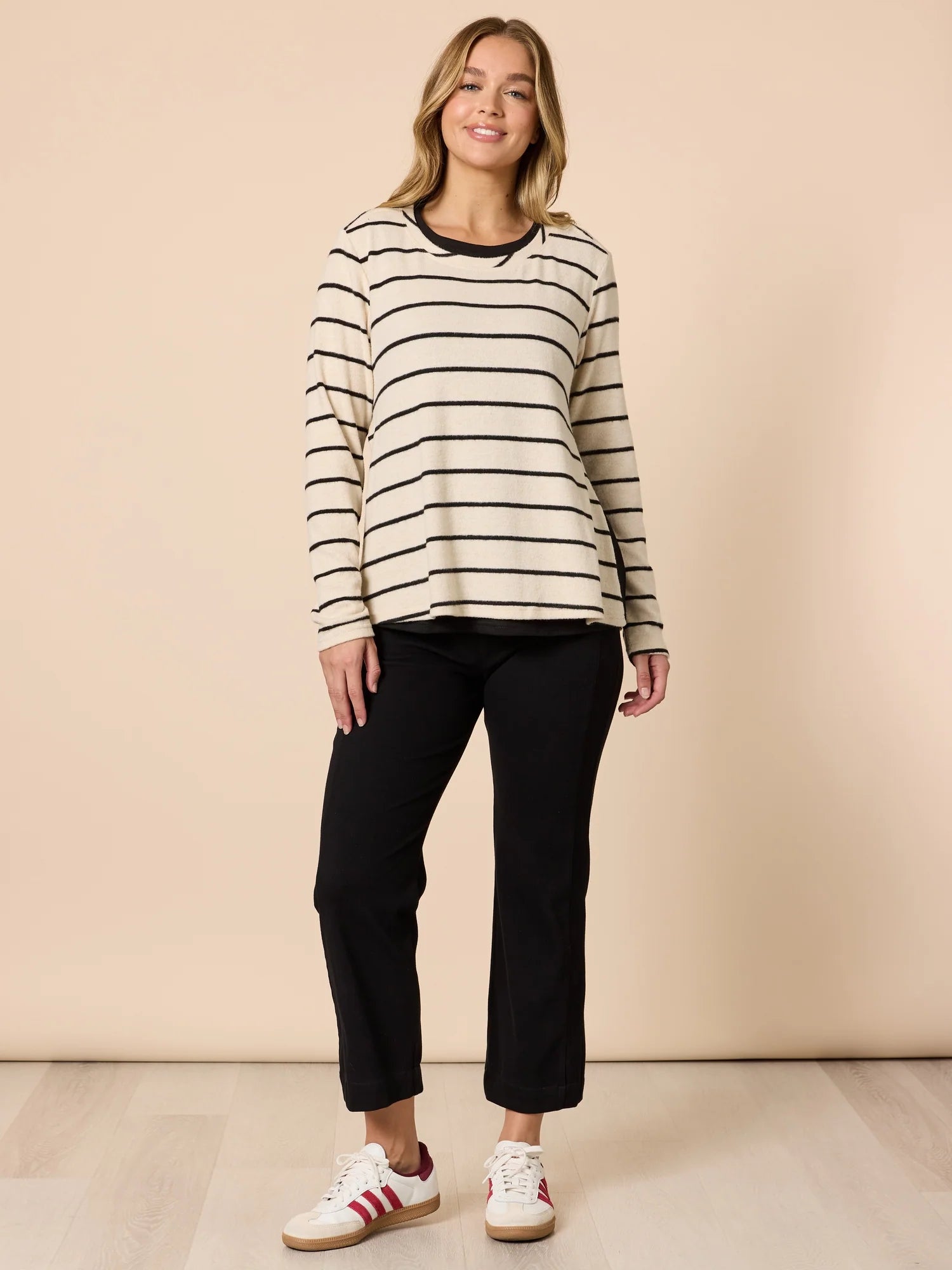 Image of Woman wearing a Threadz striped sweater and black pants against a beige background