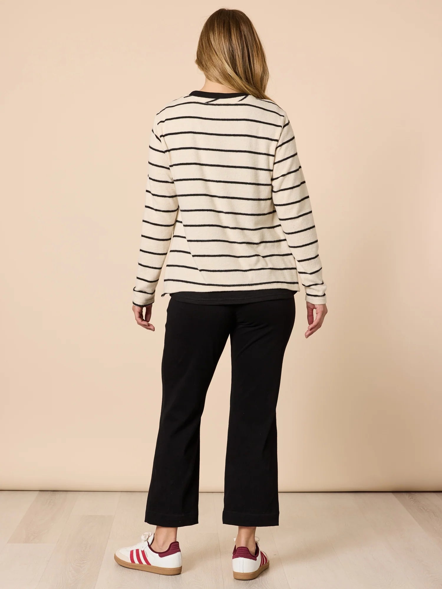 Image of Woman wearing a Threadz striped sweater and black pants on a beige background
