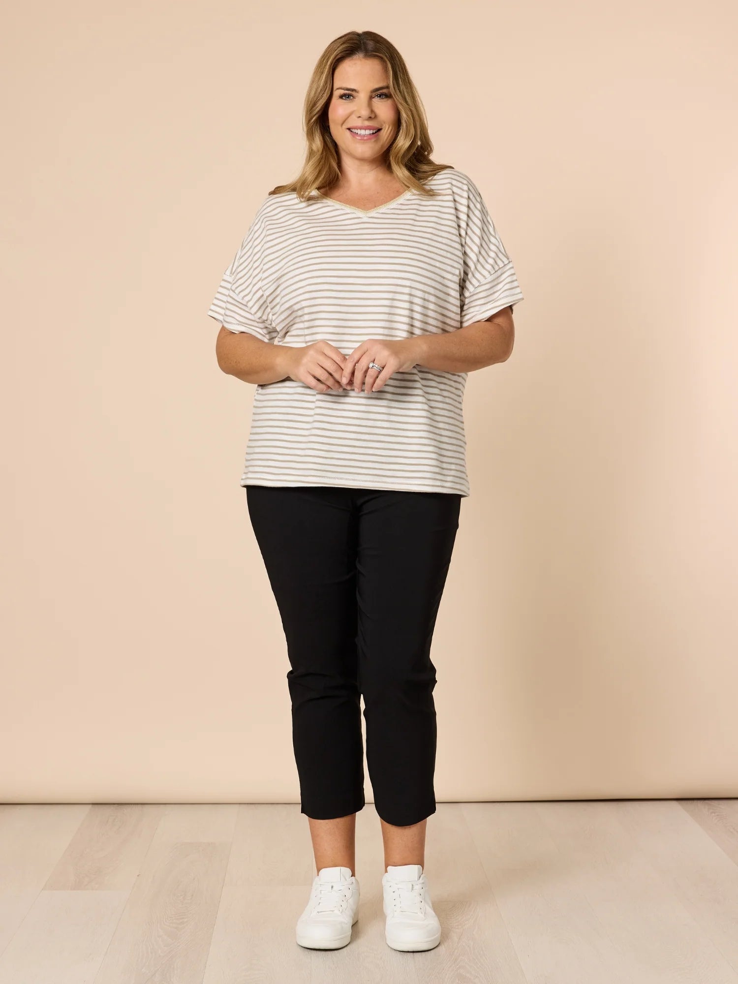 Woman wearing a striped shirt and Threadz black pants against a beige background