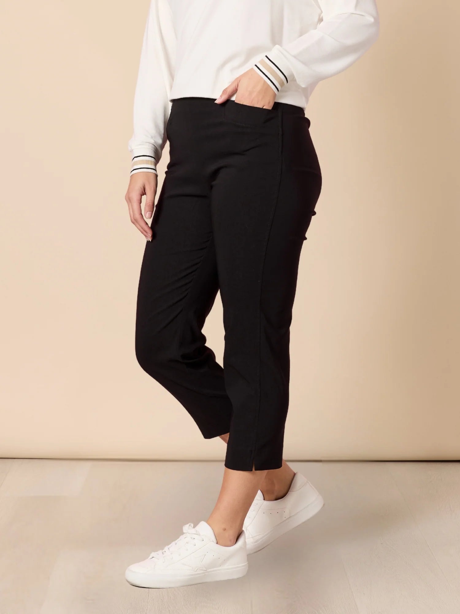 Women wearing Threadz black pants and white sneakers on a beige background