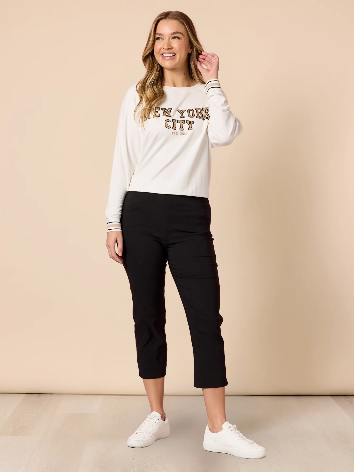 Woman wearing a white sweatshirt with text and Threadz black pants against a beige background