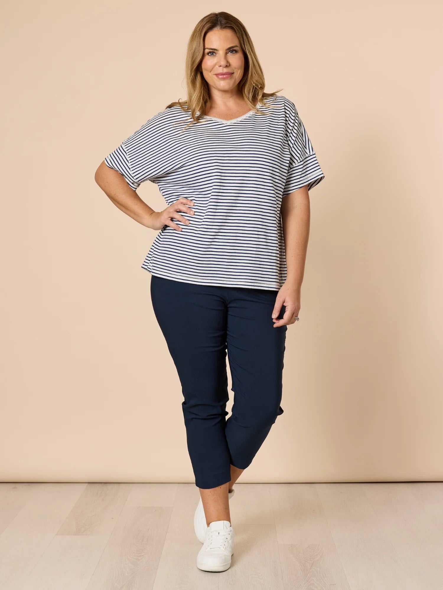 Woman wearing a striped top and Threadz navy pants against a beige background