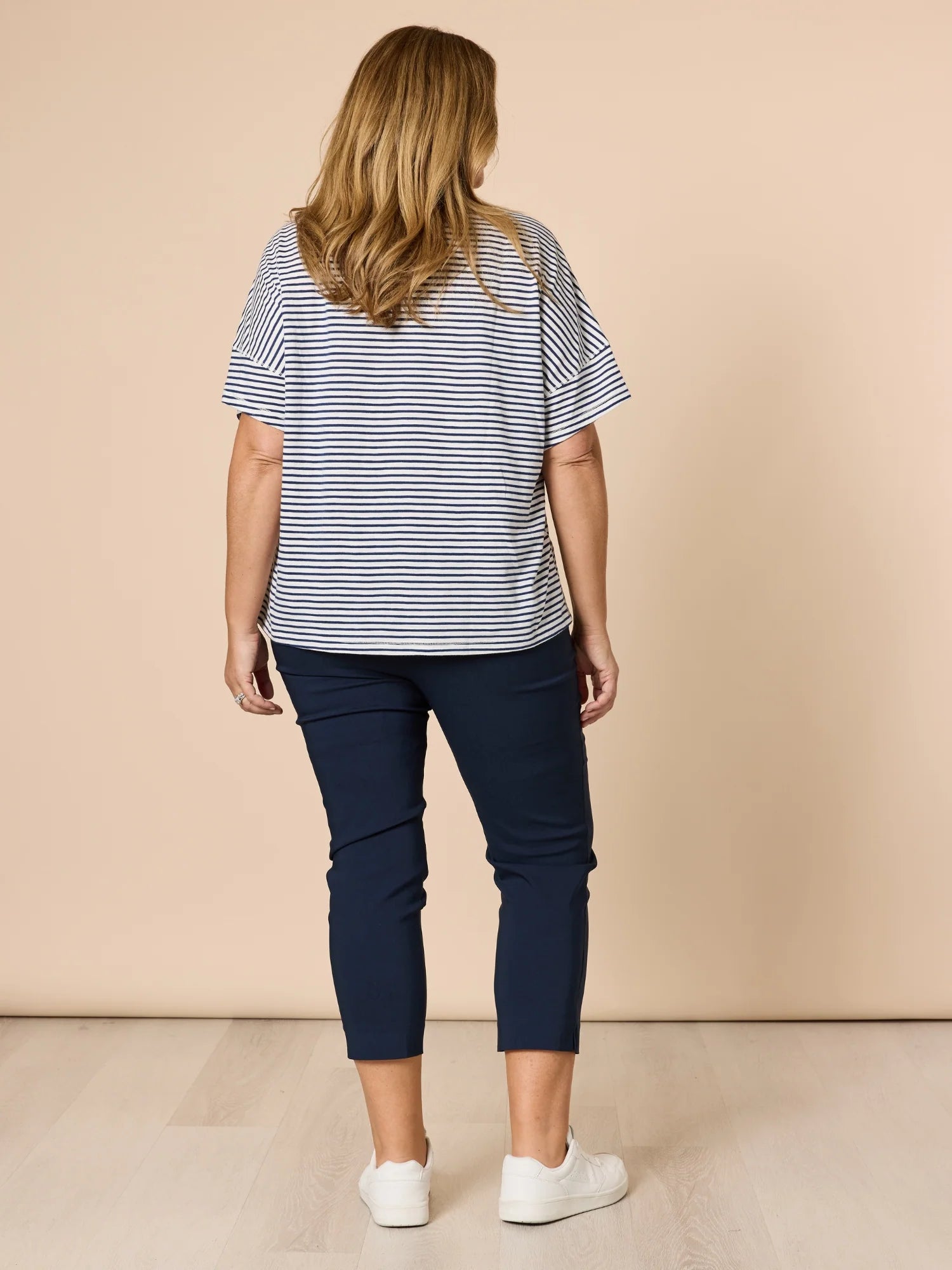 Woman wearing a striped shirt and Threadz navy pants against a beige background