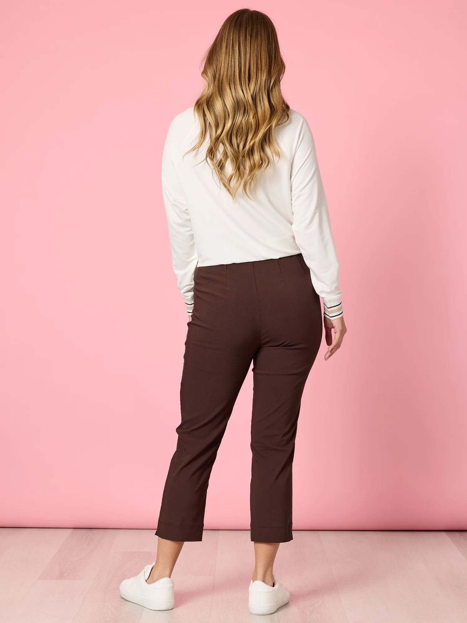 Collection of Woman wearing a white long-sleeve top and Threadz brown pants against a pink background in a gallery layout