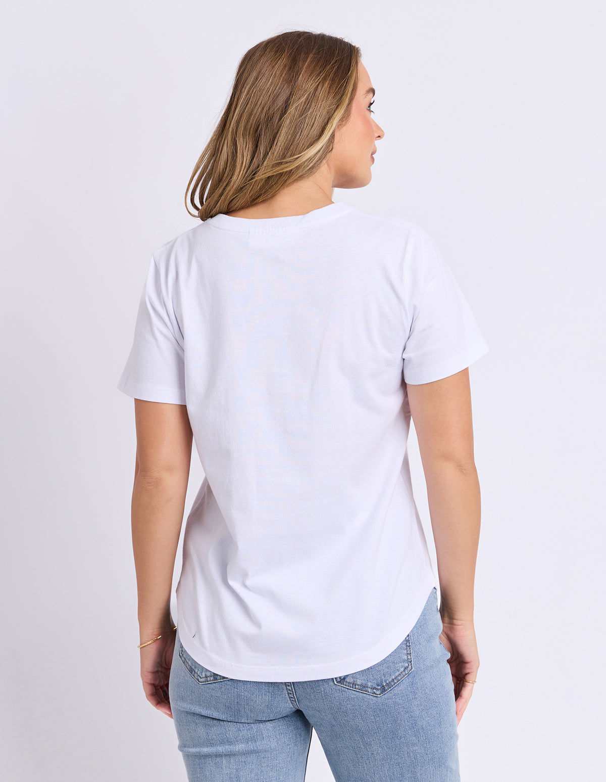 Woman wearing a plain white t-shirt and light blue jeans on a light grey background