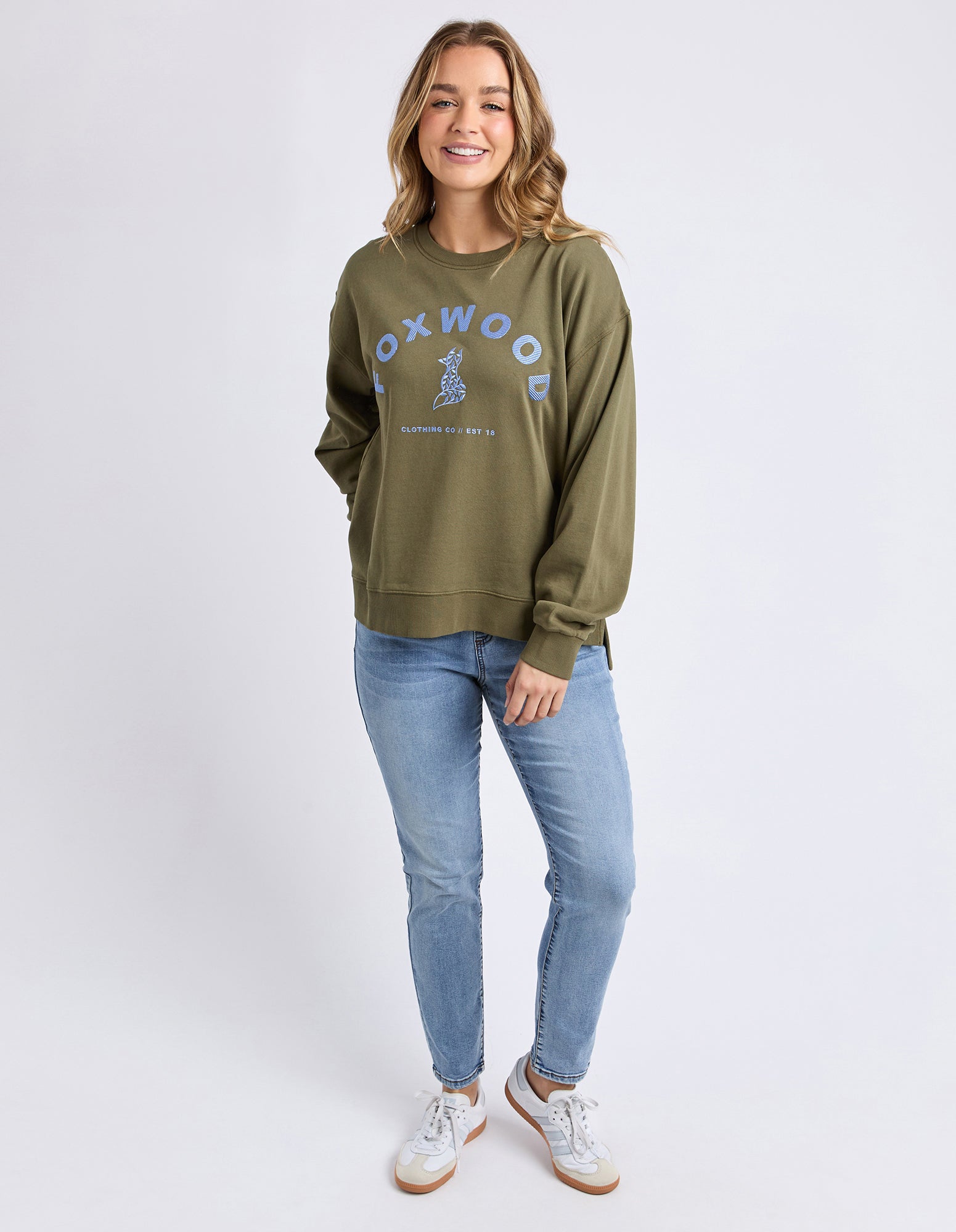 Collection of Woman wearing a green jumper with 'Foxwood' branding on a white background in a gallery layout