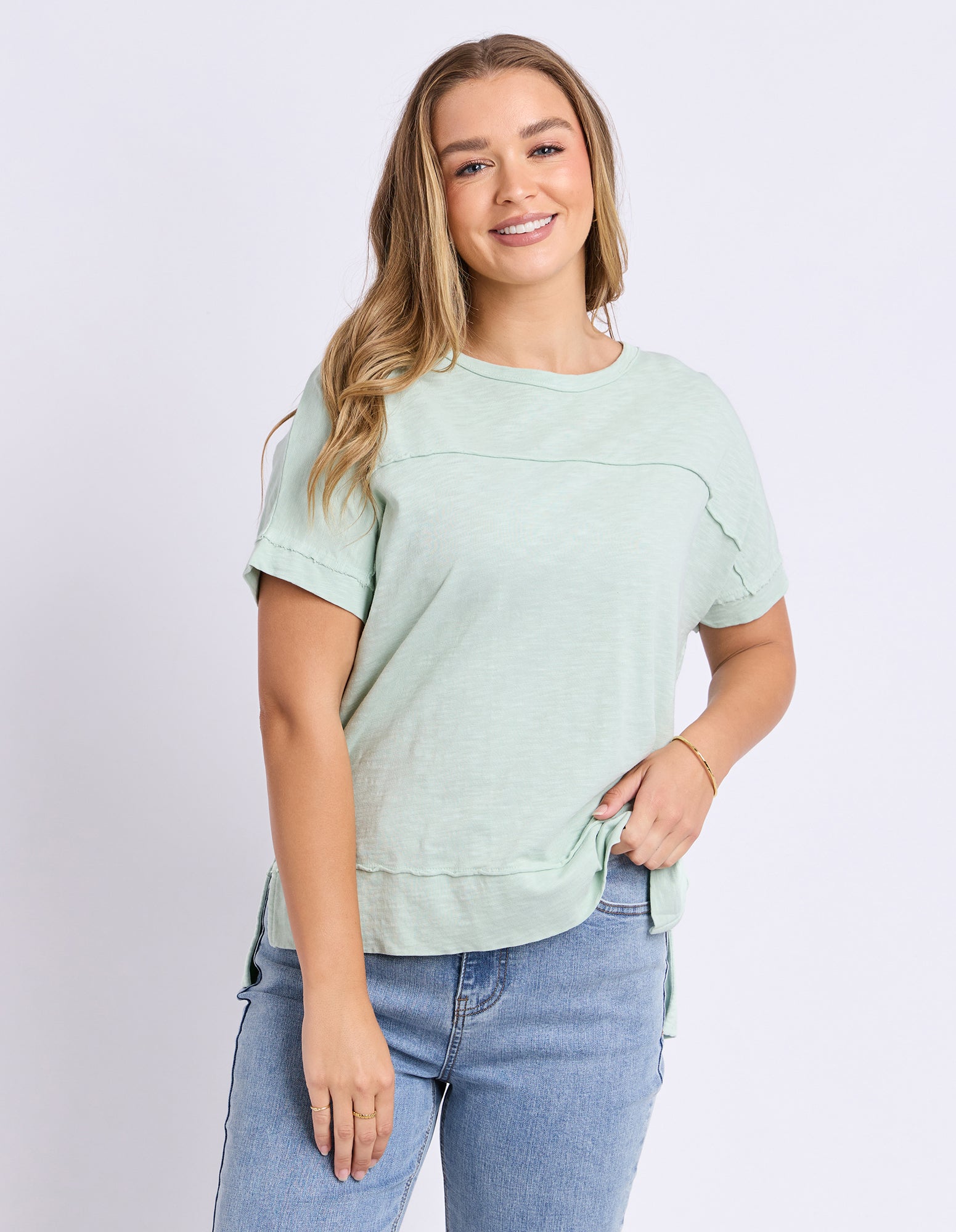 A woman modeling a light sage green tee against a light grey white background.