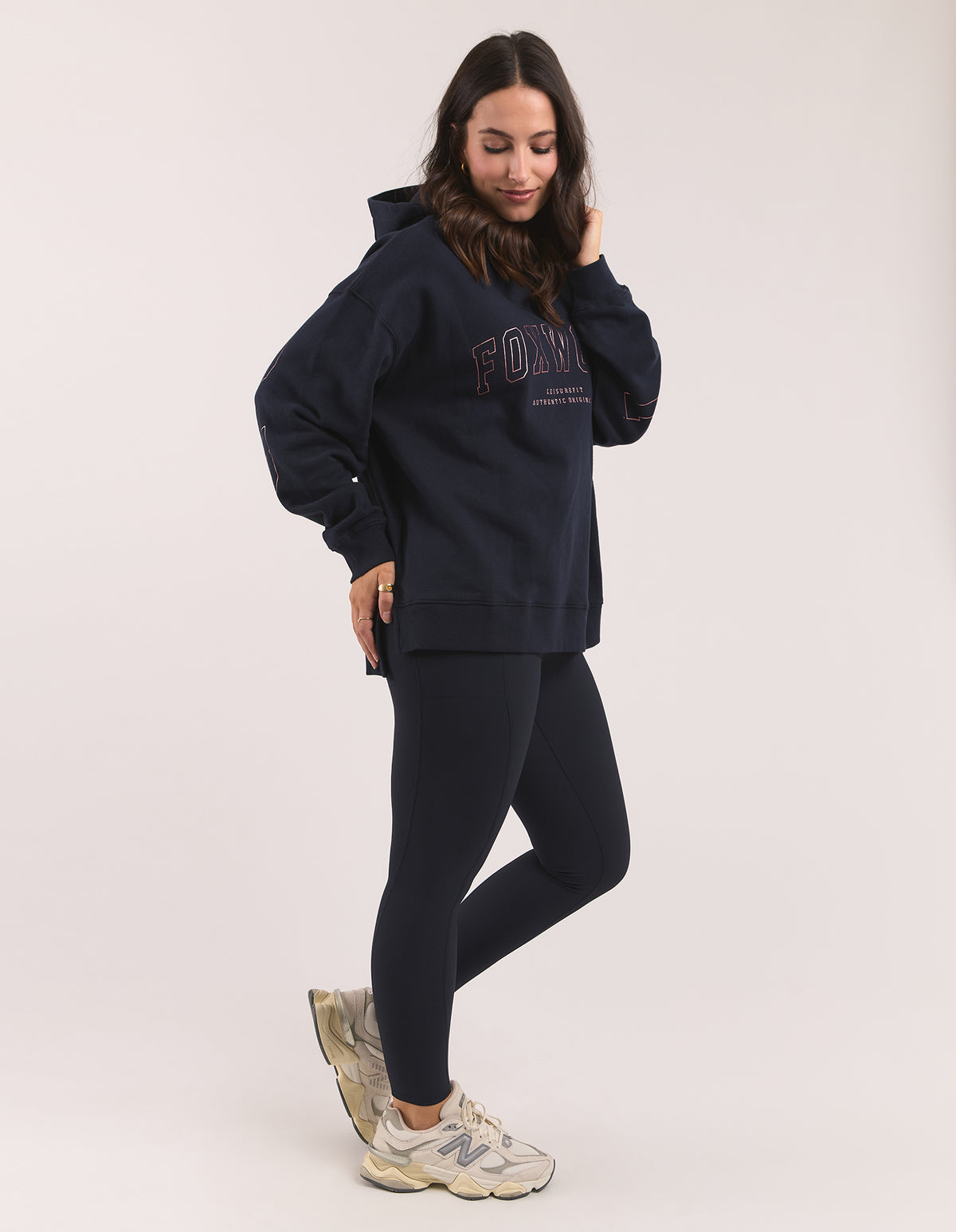 A woman modeling a navy blue hoodie with 'FOXWOOD' printed on the chest, paired with matching navy leggings and beige sneakers, against a plain light background.