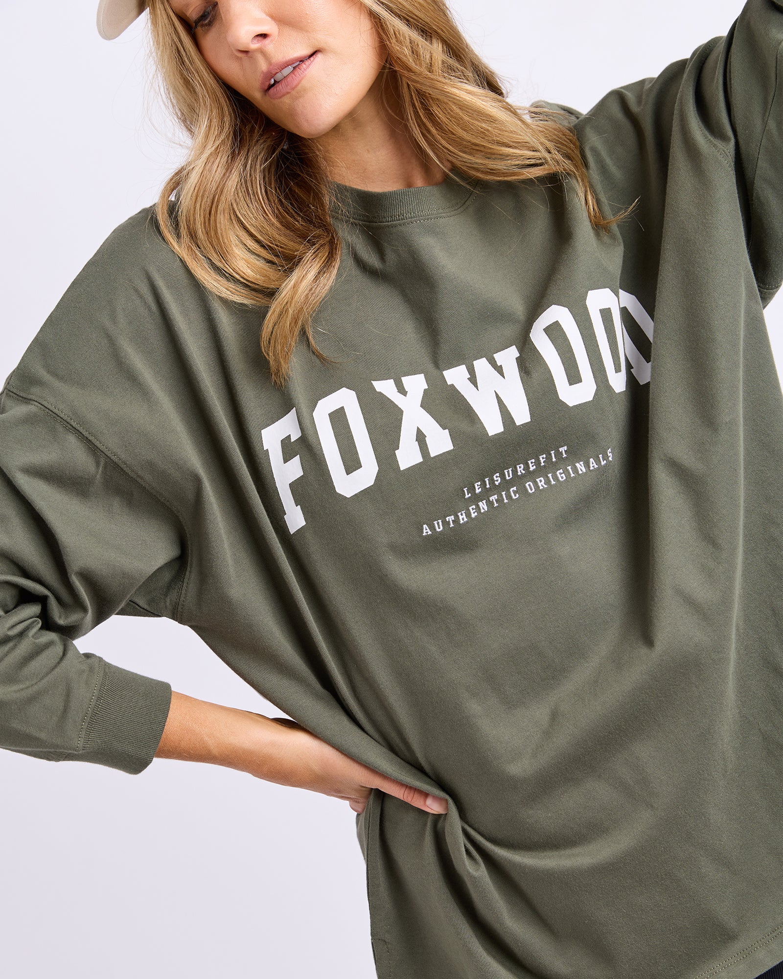 Image of blonde woman wearing a khaki long sleeve tee with 'FOXWOOD' branding on a plain background