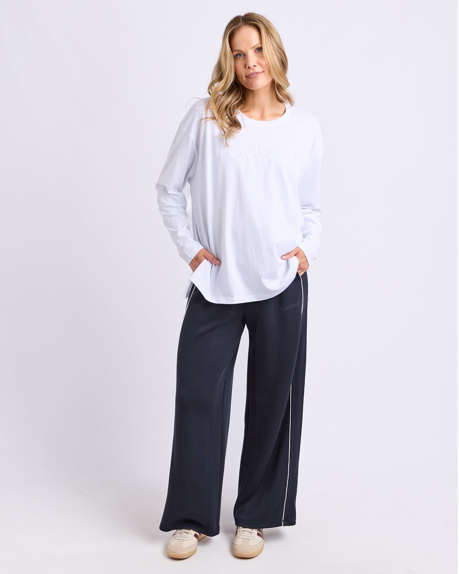 Image of Woman wearing a white Foxwood long sleeve tee and dark pants on a white background