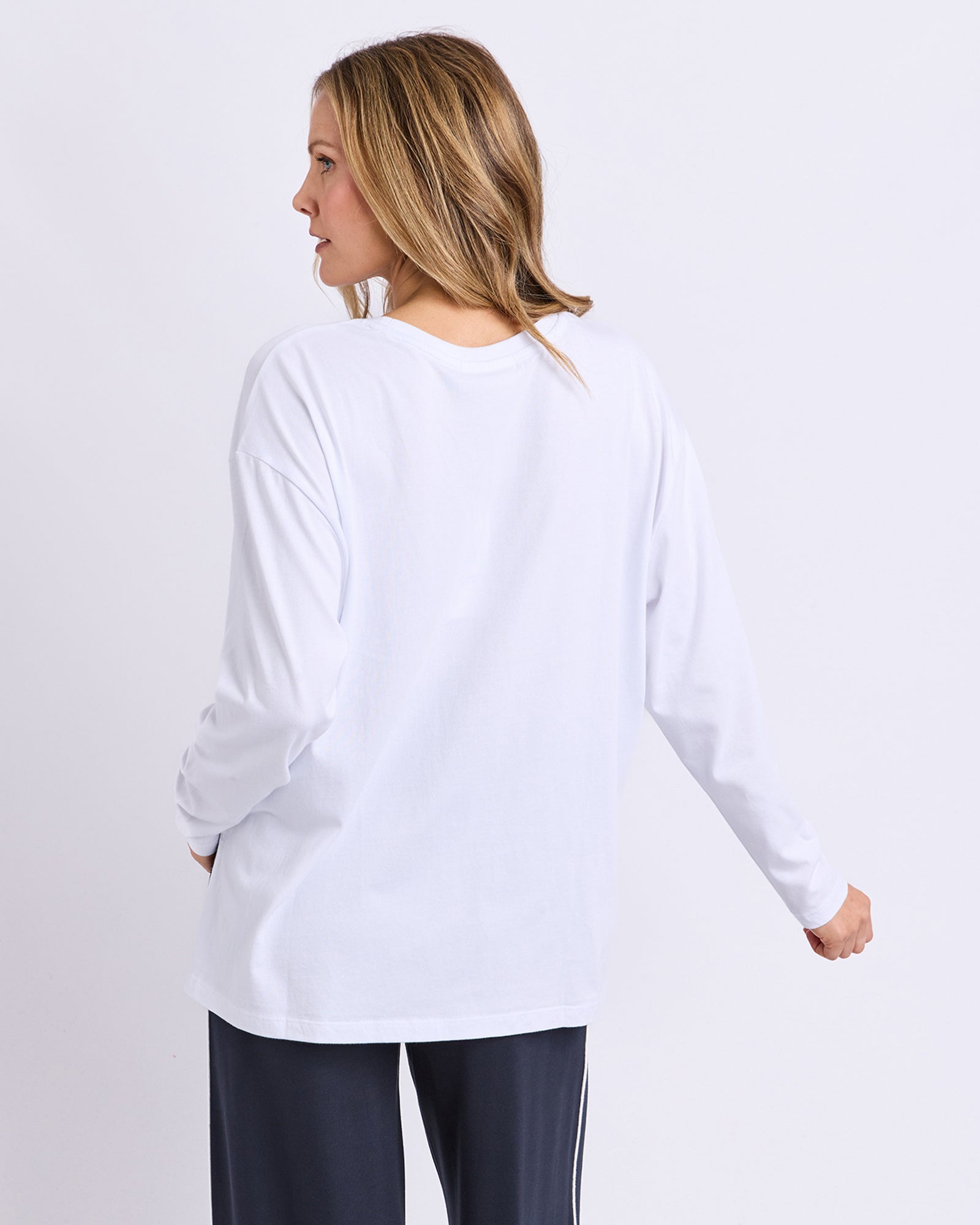 Woman wearing a white long-sleeve Foxwood top and dark pants on a light grae background