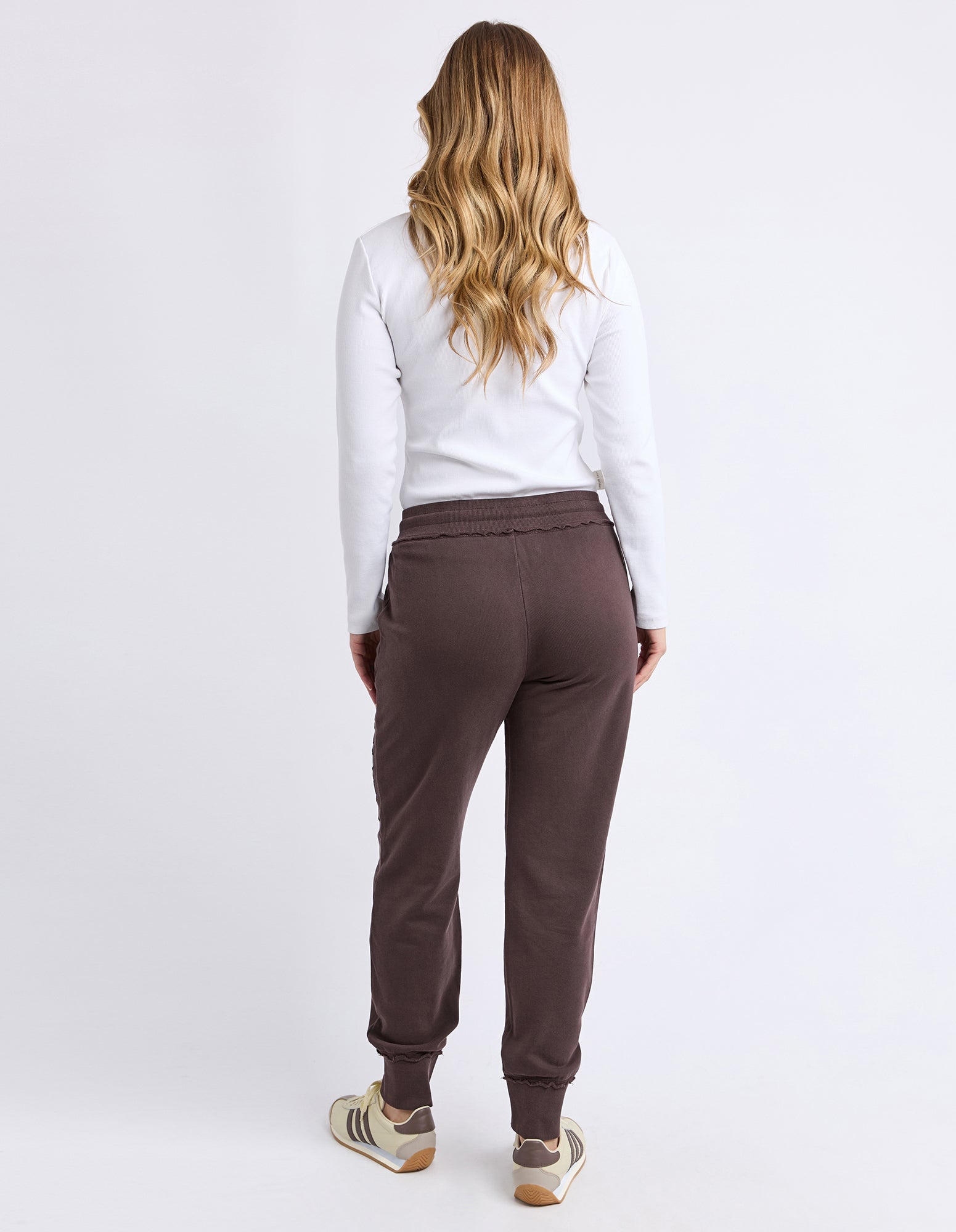Image of Woman wearing brown track pants and a white top on a plain background