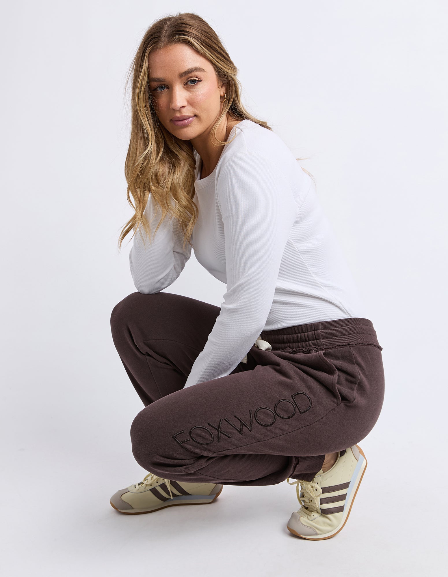 Image of Woman wearing brown 'FOXWOOD' track pants on a white background