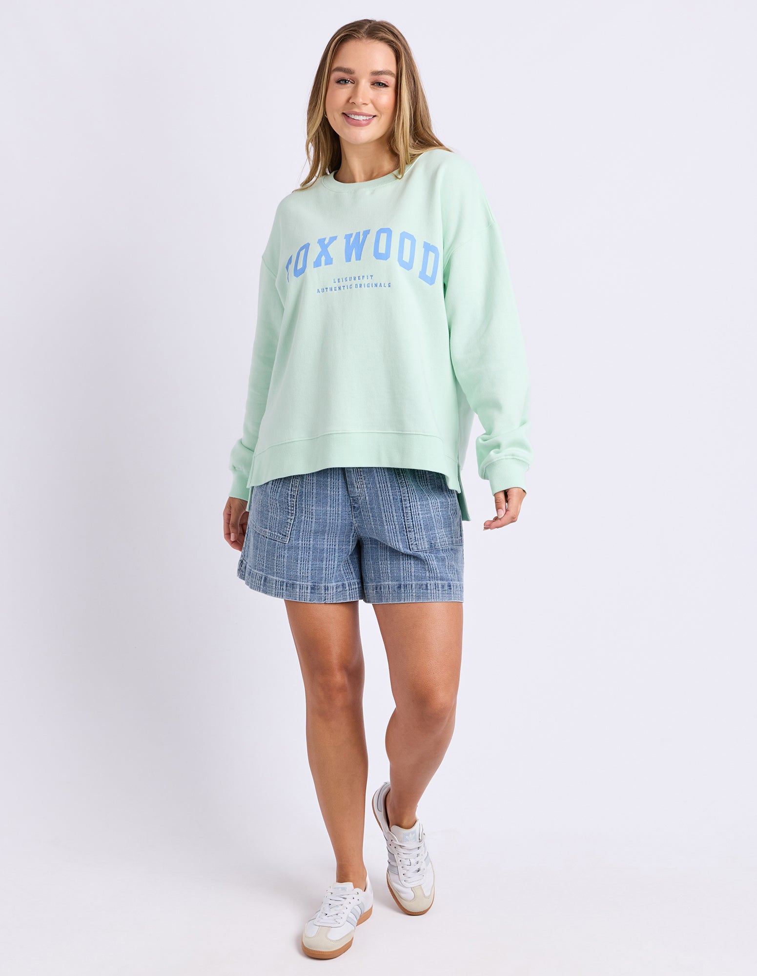 Woman wearing a mint green jumper with 'Foxwood' text in blue on a white background