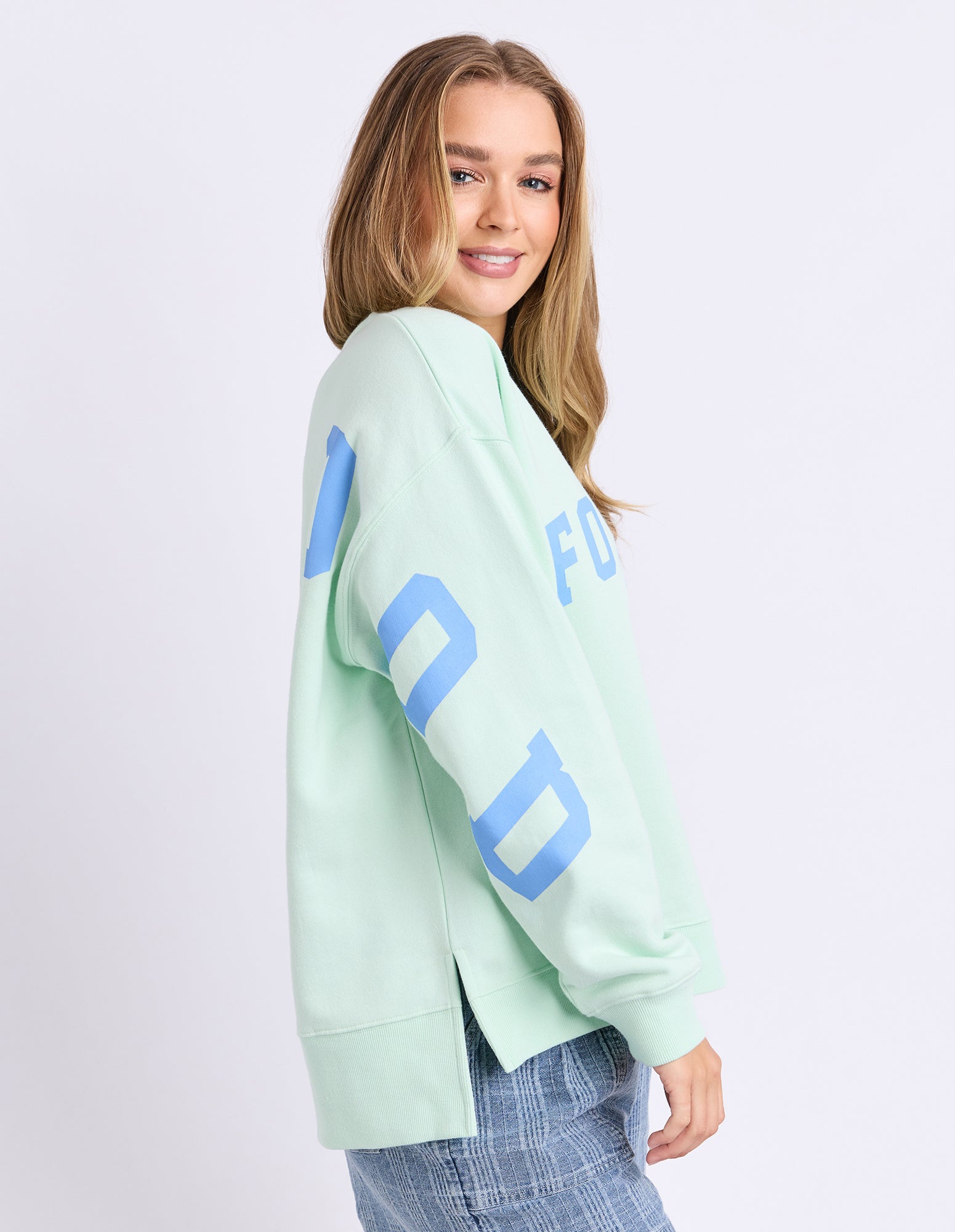 Woman wearing a mint green jumper with blue text on a white background