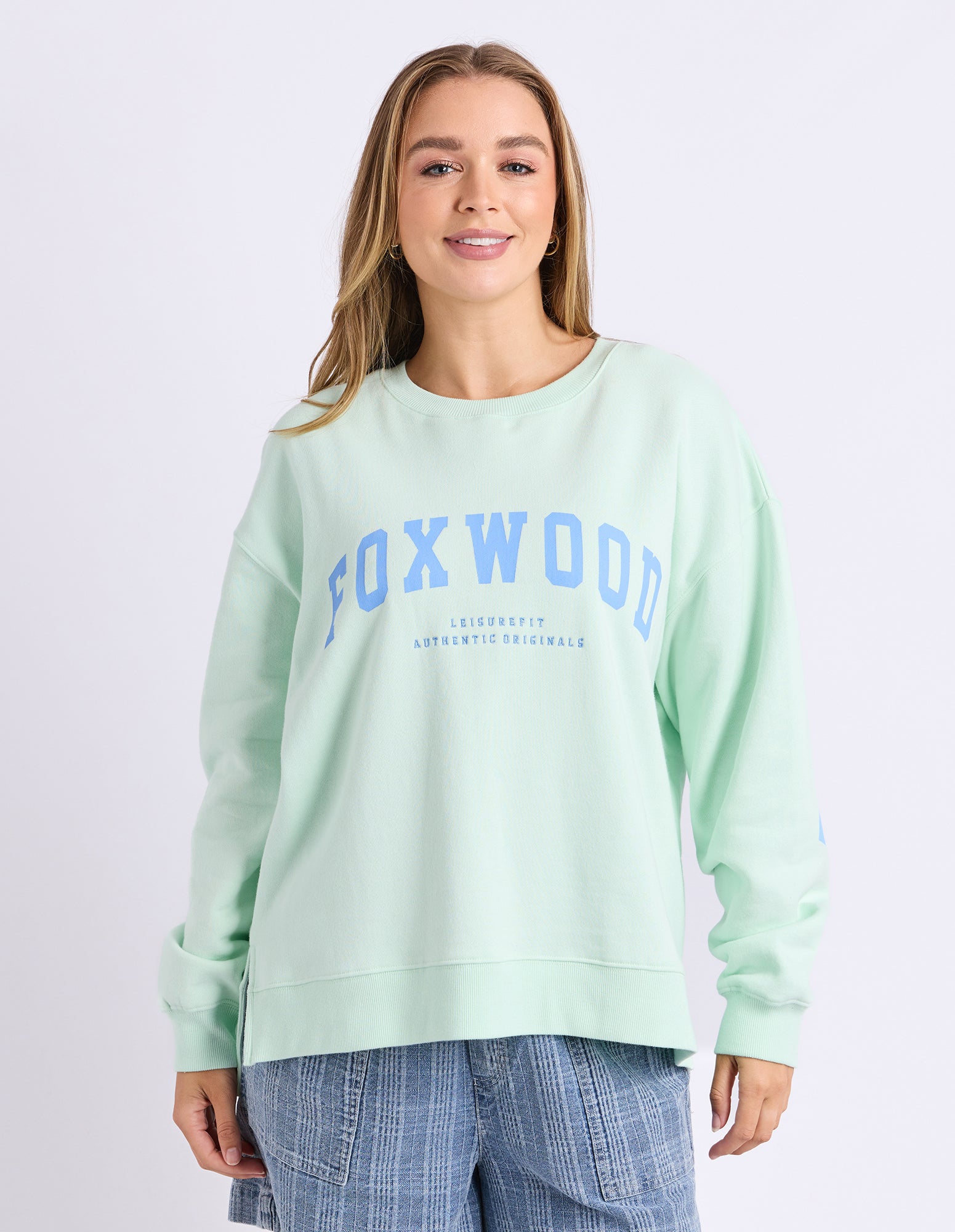 Image of Woman wearing a mint green jumper with 'FOXWOOD' printed on it in blue against a white background