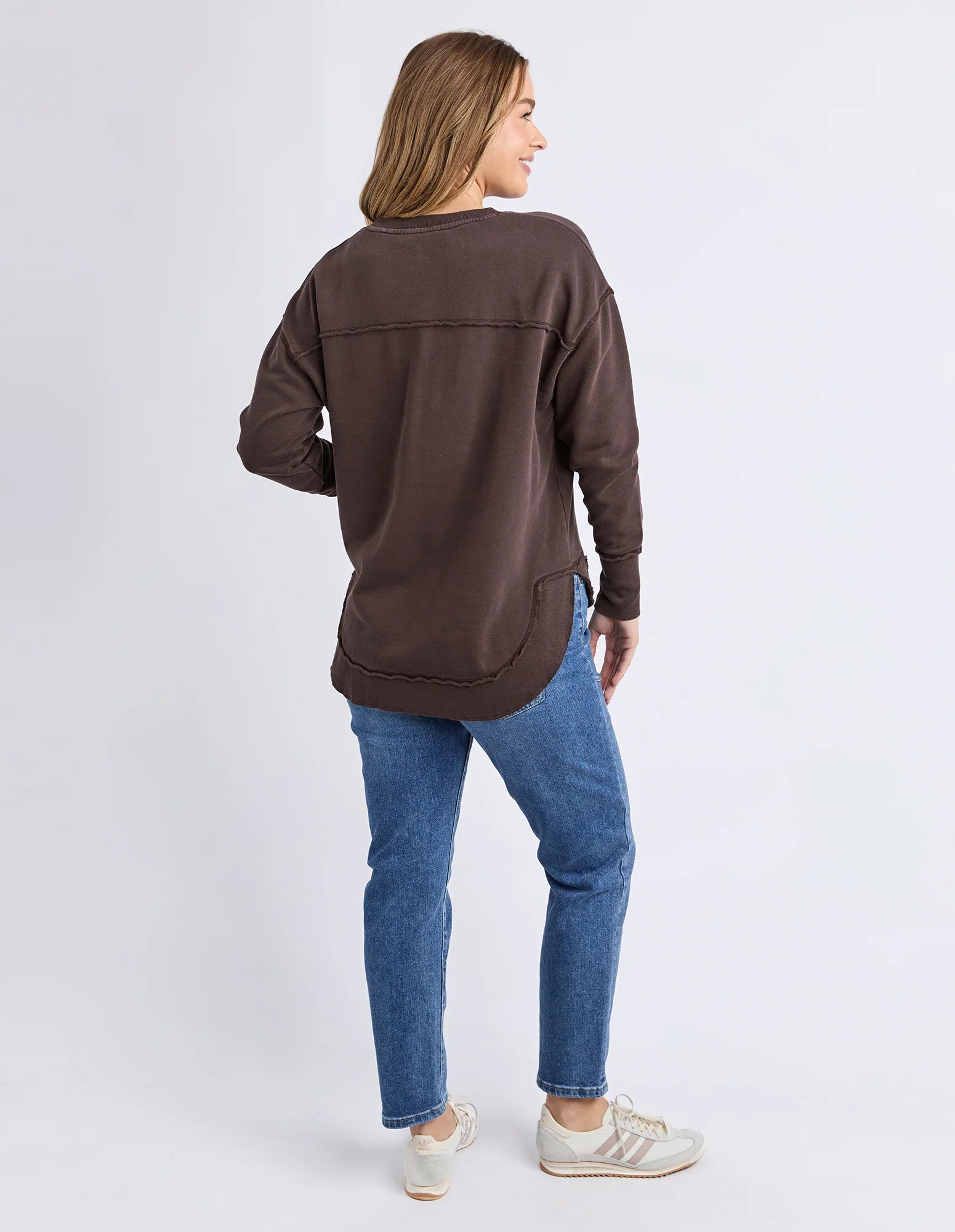 Back View of a Woman wearing a brown Foxwood jumper and blue jeans on a white background