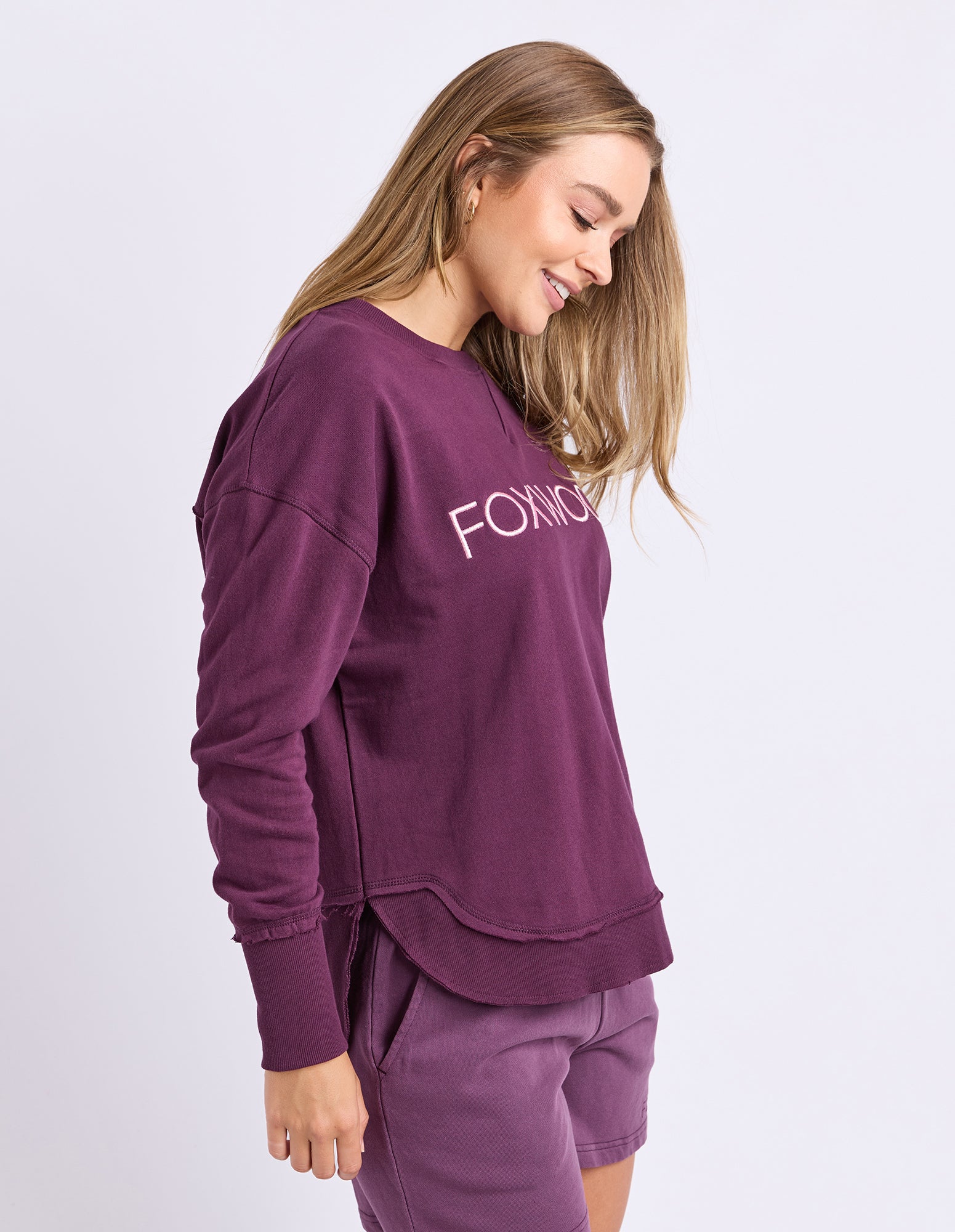 Image of A woman wearing a plum jumper with Foxwood embroidered on the chest against a light grey background.